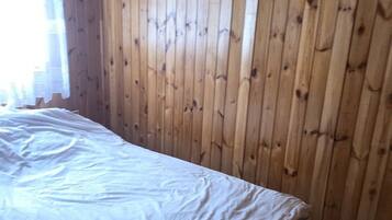 Ein Zimmer mit Holzwandverkleidung, einem Bett mit weißer Matratze und zwei gerahmten Bildern an der Wand.