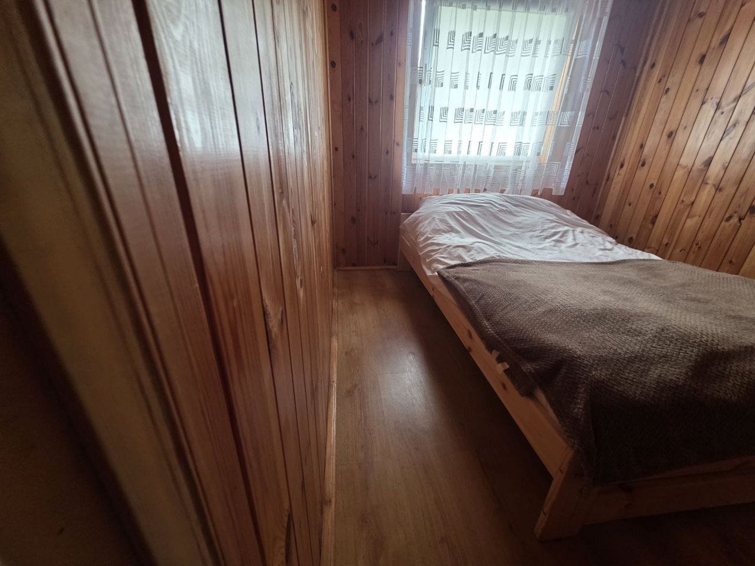 Una habitación pequeña y estrecha con paredes de madera y una cama individual.