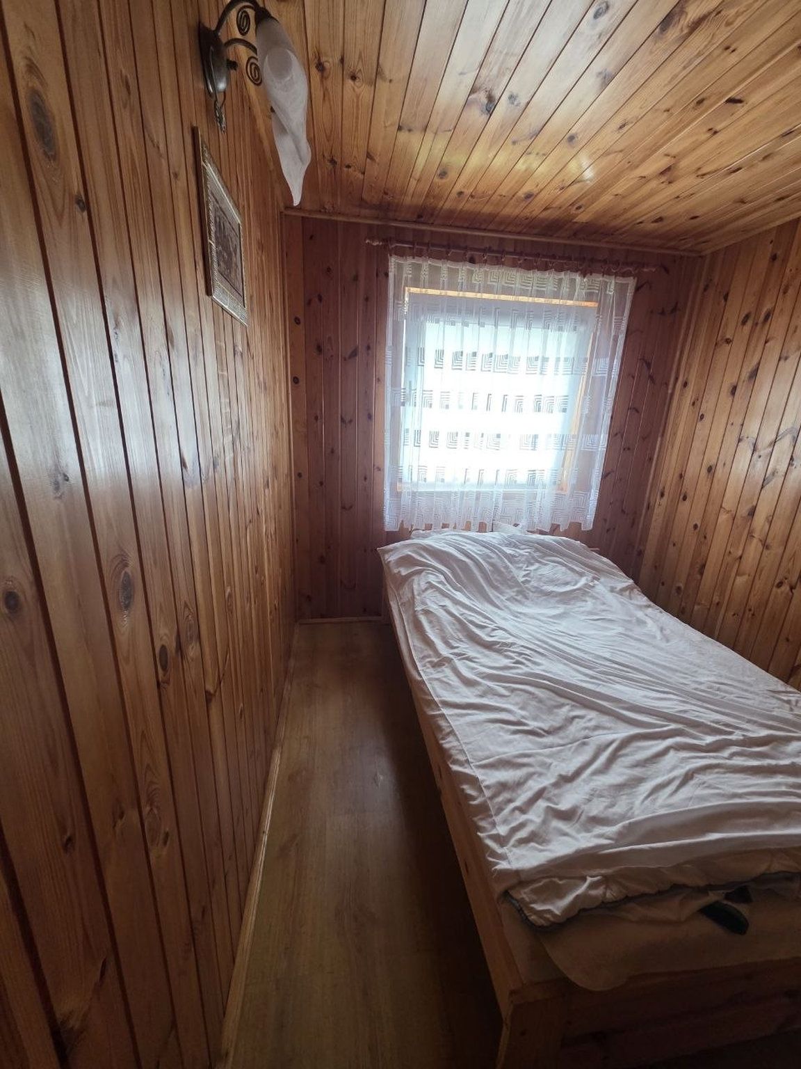 Une petite chambre avec un lit simple, des murs en bois et un plafond en pente.