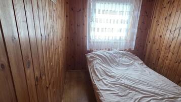 Une petite chambre avec un lit simple, des murs en bois et un plafond en pente.
