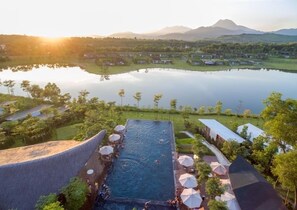An infinity pool with a view of a lake and mountains, surrounded by umbrellas and lounge chairs.