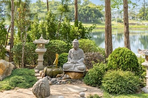 A serene garden with a Buddha statue, a stone lantern, and a pond.