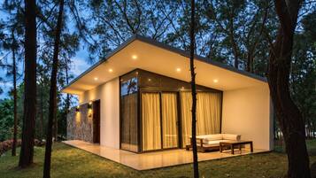 A modern house with a glass facade, a patio, and a view of the surrounding forest.
