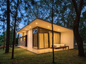 Una casa moderna con fachada de vidrio, un patio y vistas al bosque circundante.