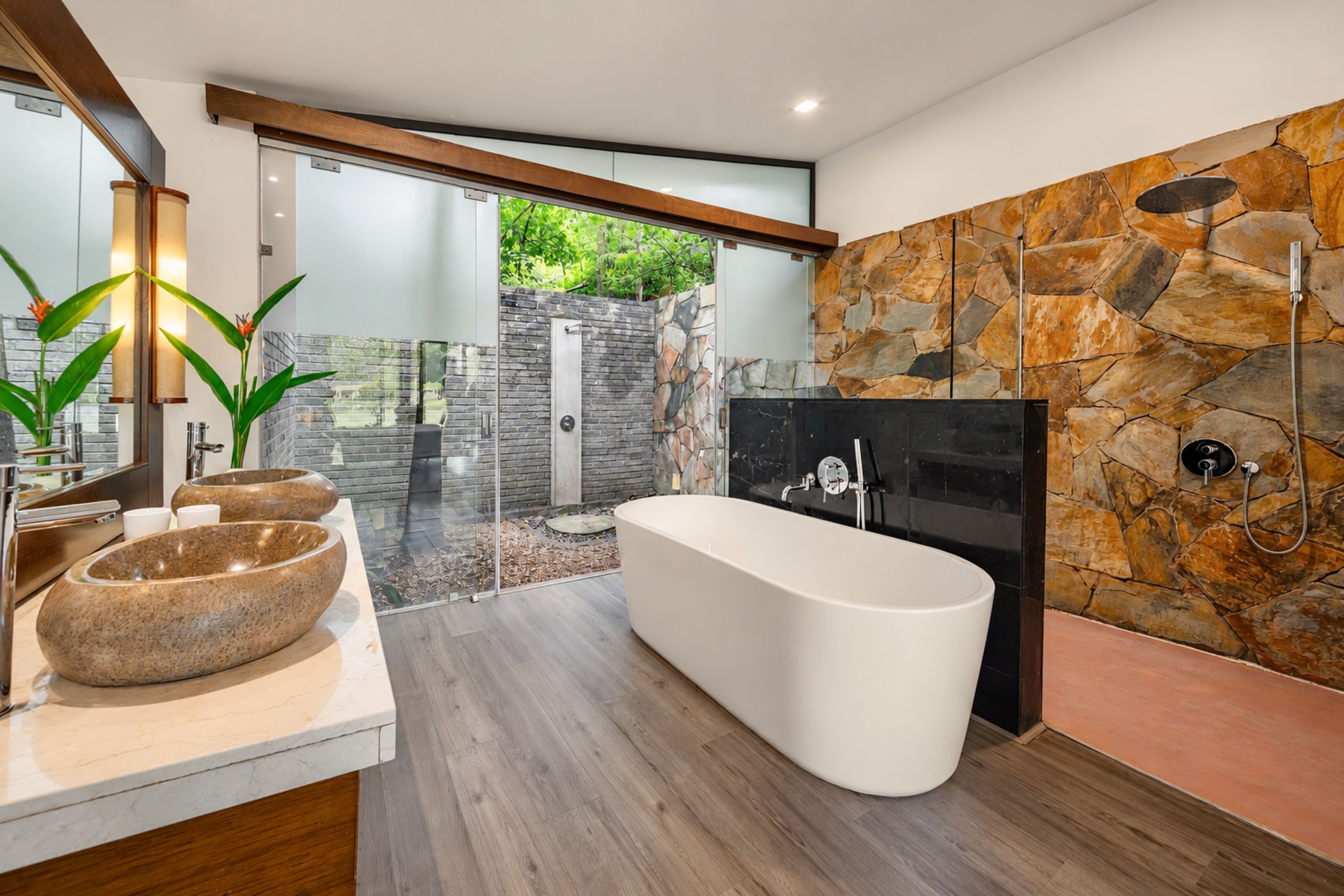 A modern bathroom with a freestanding bathtub, a stone accent wall, and a glass shower enclosure.
