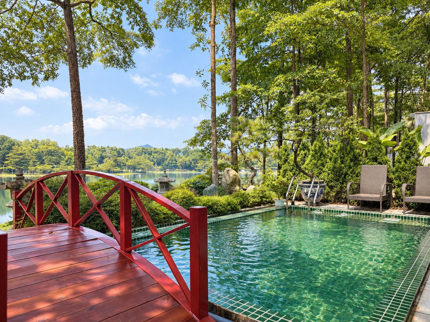 A wooden deck with a red railing leading to a clear pool surrounded by lush greenery and trees.