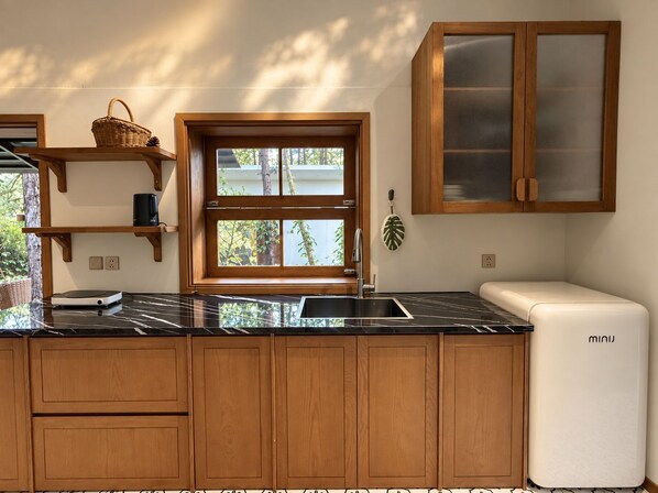A modern kitchen with wooden cabinets, a black marble countertop, a built-in sink, and a white mini fridge.