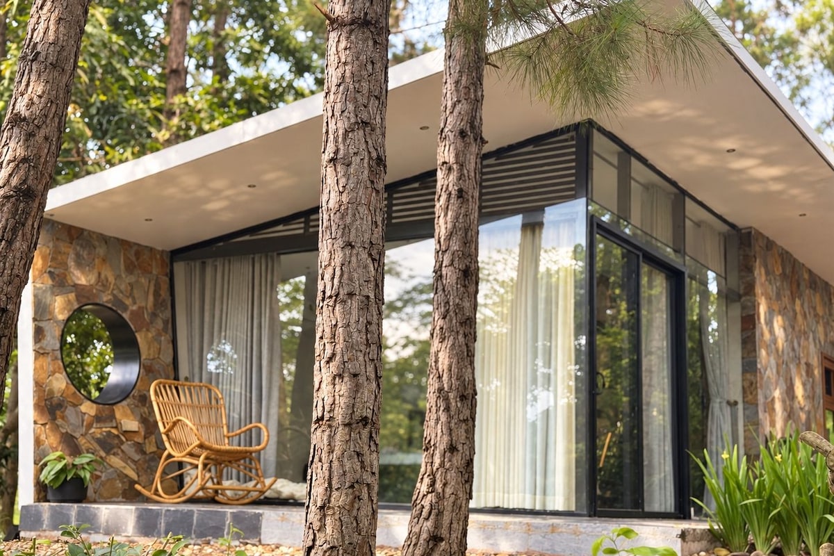 A modern house with a stone facade, large windows, and a wooden swing chair outside.
