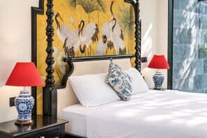A bed with white linens, two red lamps, and a decorative wall with a bird painting.