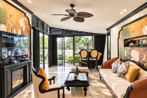A modern living room with a television, seating, a ceiling fan, and a view of the outdoors.
