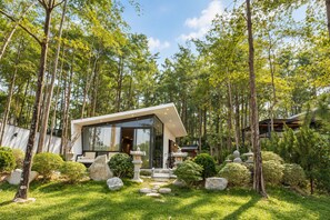 A modern house with a glass facade, surrounded by a lush garden and tall trees.