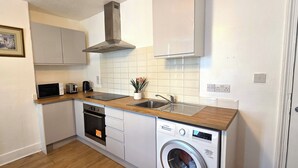 A compact kitchen with a built-in dishwasher, a microwave, a toaster, and a sink. - Apartment Sleeps 2 With Garden (Clacton-on-Sea)