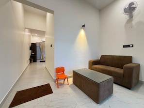 A modern living room with a sofa, a glass coffee table, and a small orange chair. - KUNA RESORT (Allampura)