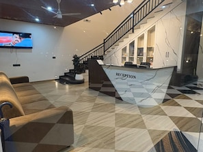 A reception area with a marble counter, a staircase, and a television mounted on the wall. - KUNA RESORT (Allampura)