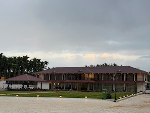 A two-story building with a flat roof, a covered outdoor area with seating, and a paved walkway.