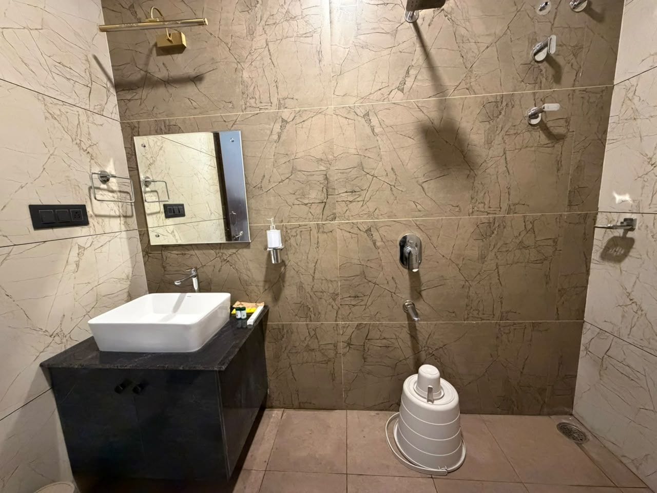 Un baño con lavamanos blanco, encimera negra y ducha con recipiente blanco.