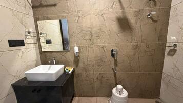 Un baño con lavamanos blanco, encimera negra y ducha con recipiente blanco.