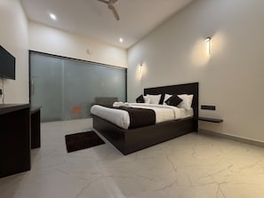A modern bedroom with a large bed, a desk, and a glass door leading to a balcony. - KUNA RESORT (Allampura)