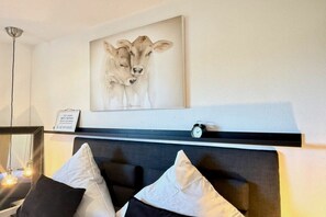 Ein Schlafzimmer mit einem Kopfteil, einem Nachttisch, einer Lampe, einer Uhr und einem gerahmten Bild einer Kuh.