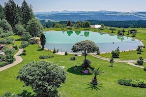Ein großer, kreisrunder Teich, umgeben von gepflegten Rasenflächen und Bäumen, mit freiem Blick auf ferne Berge.