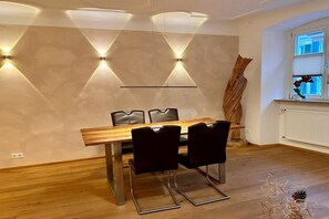 Ein Essbereich mit einem Holztisch und vier Stühlen, einer dekorativen Wand mit integrierter Beleuchtung und einem Fenster mit Jalousien.