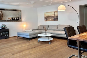 Ein modernes Wohnzimmer mit einem Ecksofa, einem runden Couchtisch und einem Essbereich mit Holztisch und Stühlen.