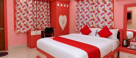 A hotel room with a bed, a desk, a chair, a heart-shaped wall decoration, and a red and white color scheme.