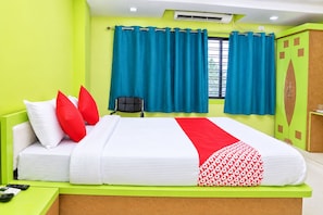 Ein Hotelzimmer mit einem Bett, einem Schreibtisch mit Telefon, einem Sessel und einem Fenster mit Vorhängen.