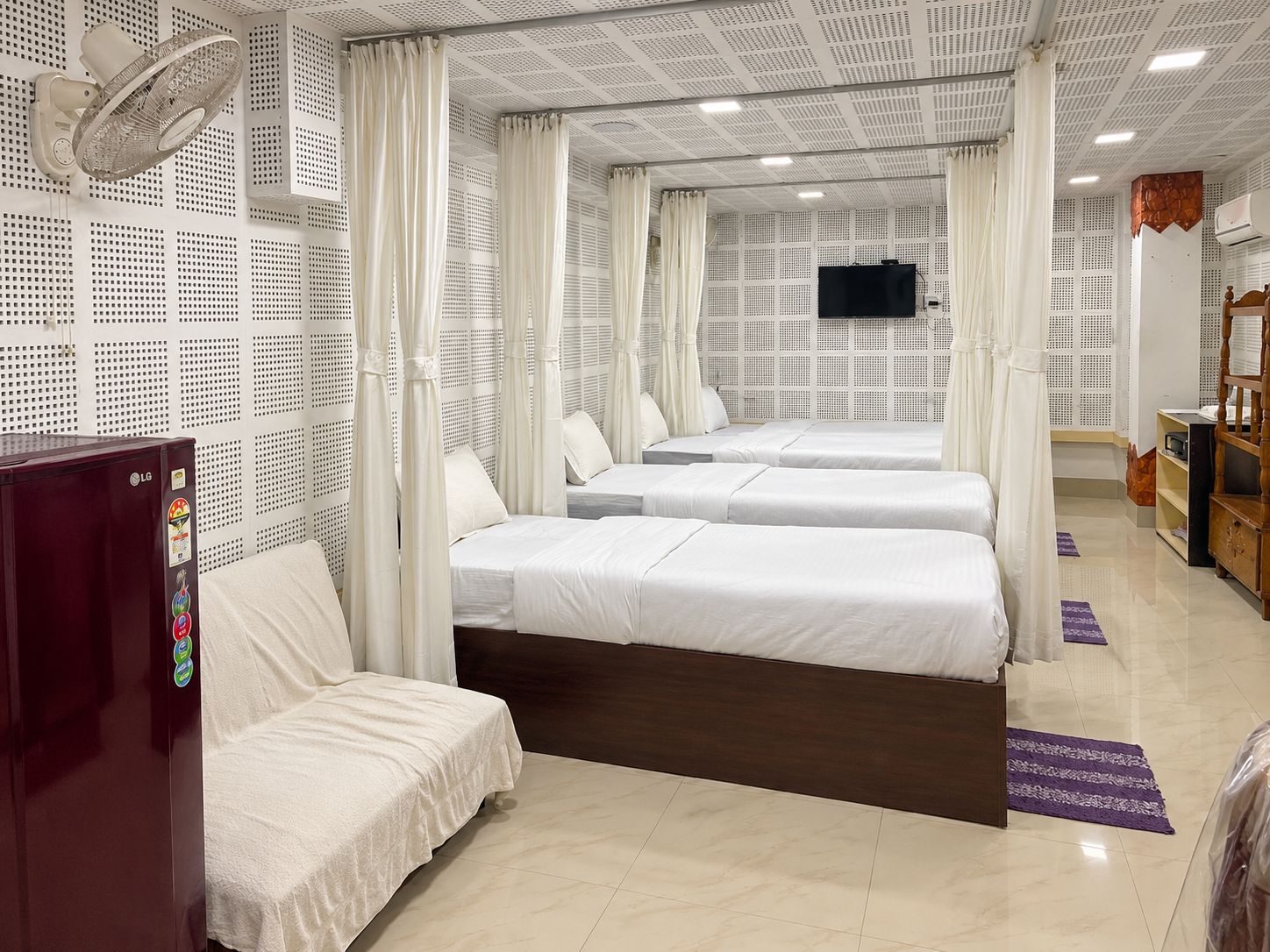 Una habitación de hotel con cama, televisión, armario y ventilador de techo.