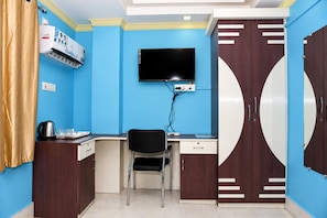 Una habitación con escritorio, silla, televisor, armario y aire acondicionado.
