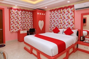 Ein Hotelzimmer mit einem Bett, einem Schreibtisch, einem Stuhl, einer herzförmigen Wanddekoration und einer roten und weißen Farbgebung.