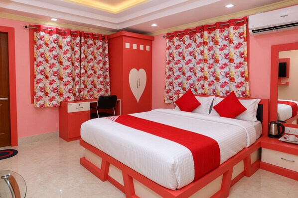 A hotel room with a bed, a desk, a chair, a heart-shaped wall decoration, and a red and white color scheme.
