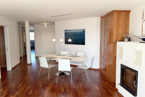 A modern dining area with a round table, white chairs, pendant lighting, and a large painting on the wall. - Holiday apartment with 1 bedroom (Nonnenhorn)