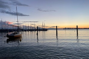 A marina with boats docked at wooden piers, calm water, and a sunset in the background. - Holiday apartment with 1 bedroom (Nonnenhorn)