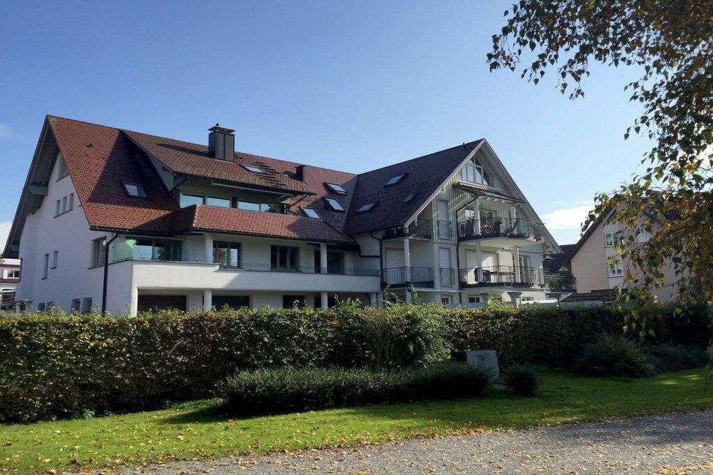 A multi-story residential building with a sloped roof, large windows, and a well-maintained garden.