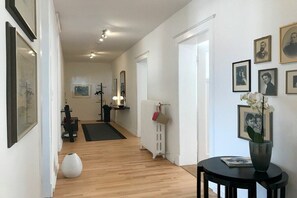 Ein Flur mit Heizkörper, gerahmten Bildern an der Wand und einem runden Tisch mit einer Vase.