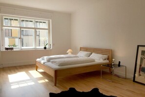 A bedroom with a wooden bed, a bedside table, a lamp, and a window with blinds. - Holiday apartment with 1 bedroom (Lindau)