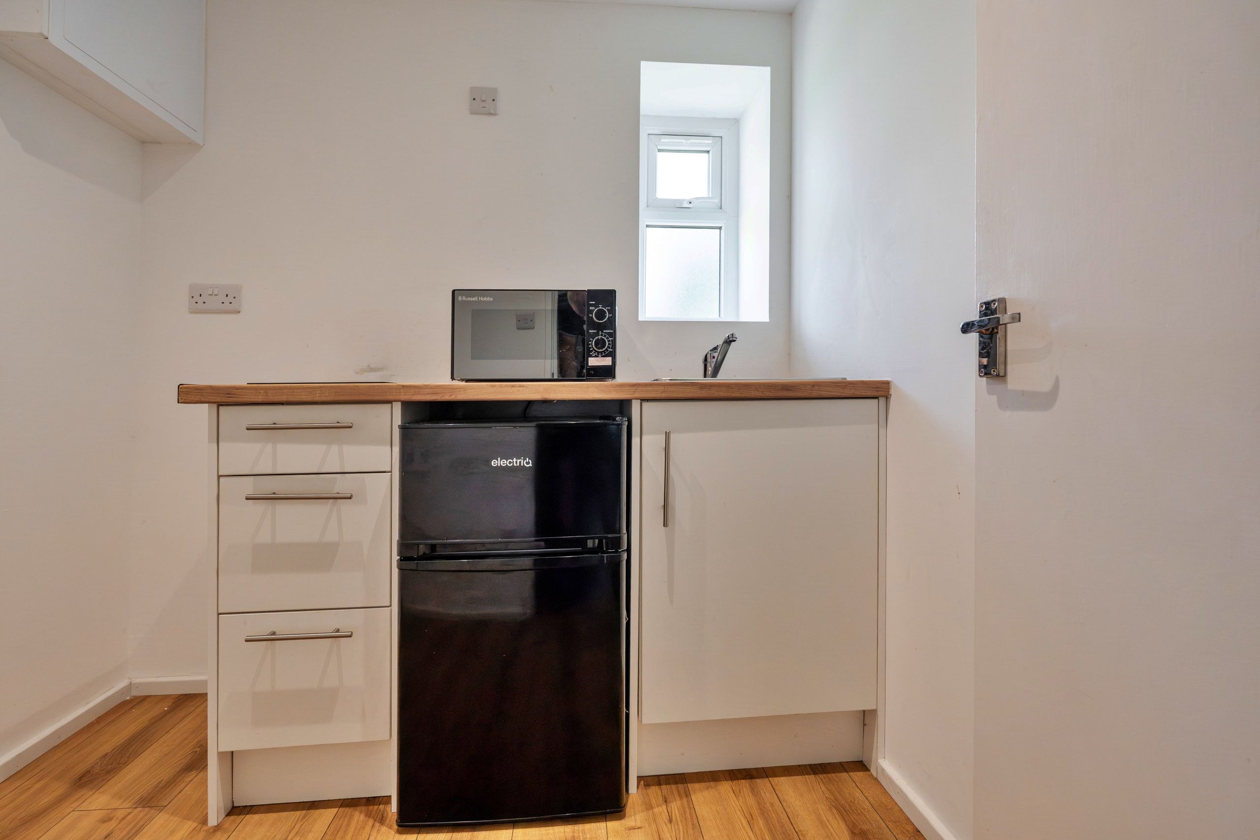 Une cuisine de taille réduite, avec un réfrigérateur noir, un four à micro-ondes et un plan de travail en bois.