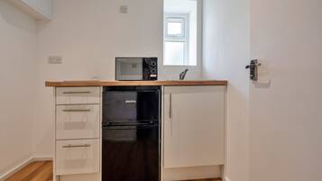 Une cuisine de taille réduite, avec un réfrigérateur noir, un four à micro-ondes et un plan de travail en bois.