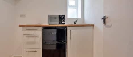 A compact kitchen with a black refrigerator, a microwave, and a wooden countertop.