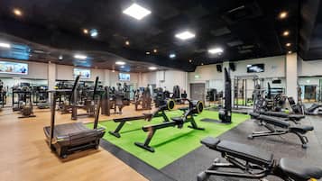 Ein Fitnessstudio mit verschiedenen Trainingsgeräten, darunter Laufbänder, Kraftgeräte und Kurzhanteln.
