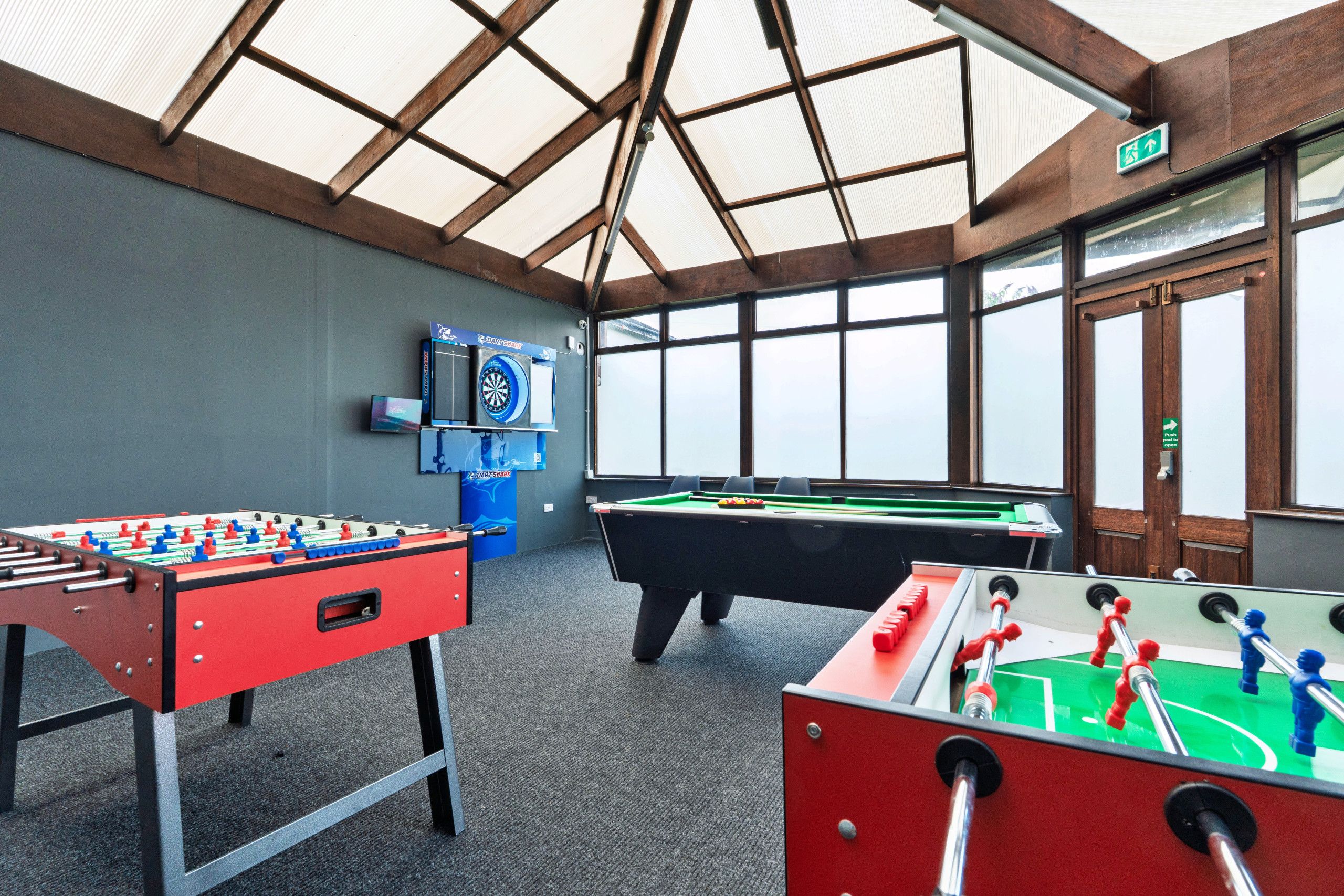 Una habitación con dos mesas de futbolín, una mesa de billar y un dardo.