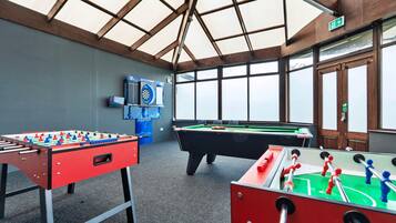 Una habitación con dos mesas de futbolín, una mesa de billar y un dardo.