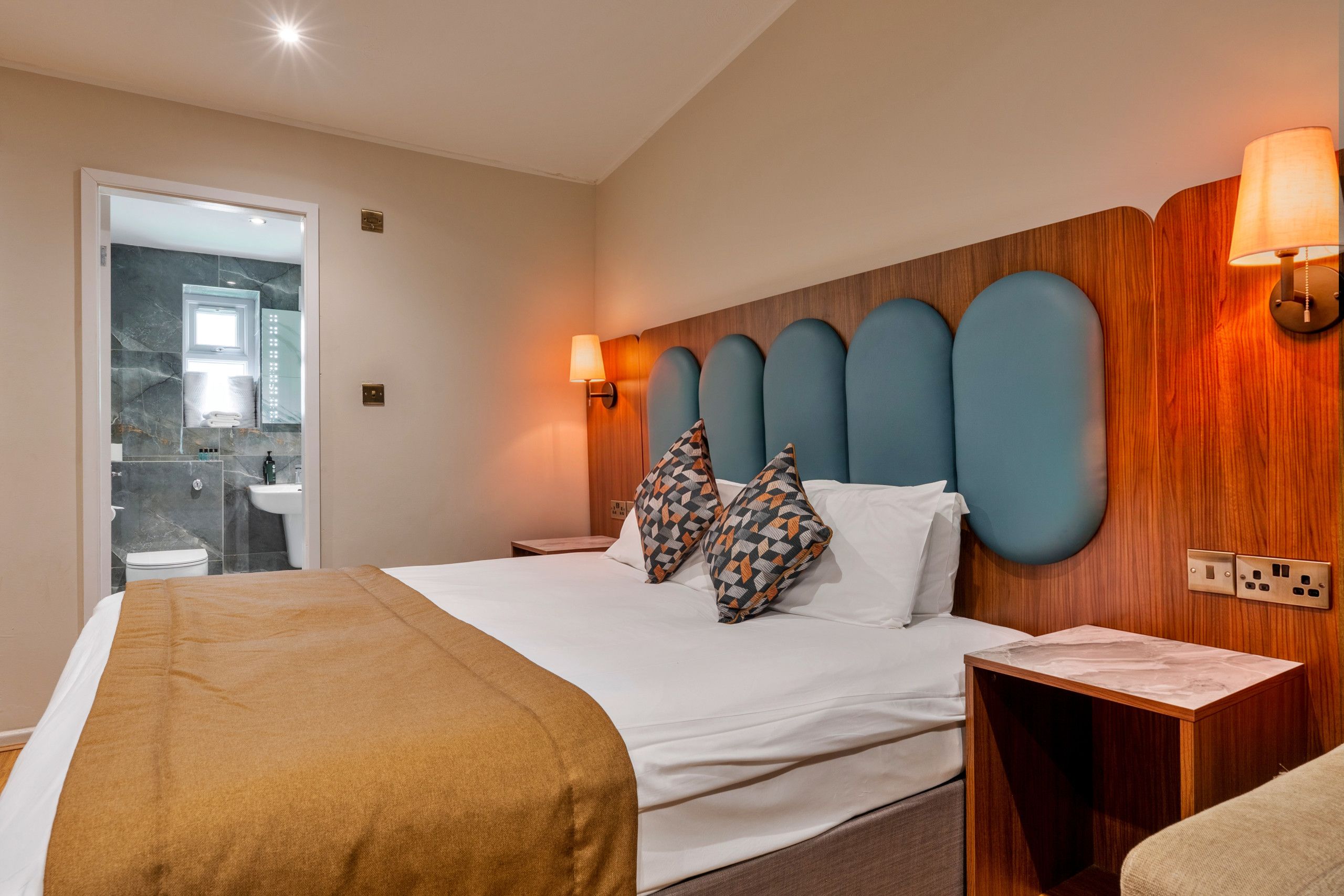 Habitación de hotel con cama, mesita de noche y baño visible a través de una puerta abierta.