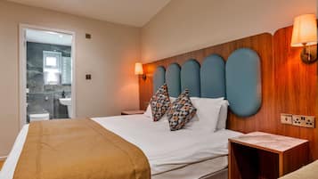 Habitación de hotel con cama, mesita de noche y baño visible a través de una puerta abierta.