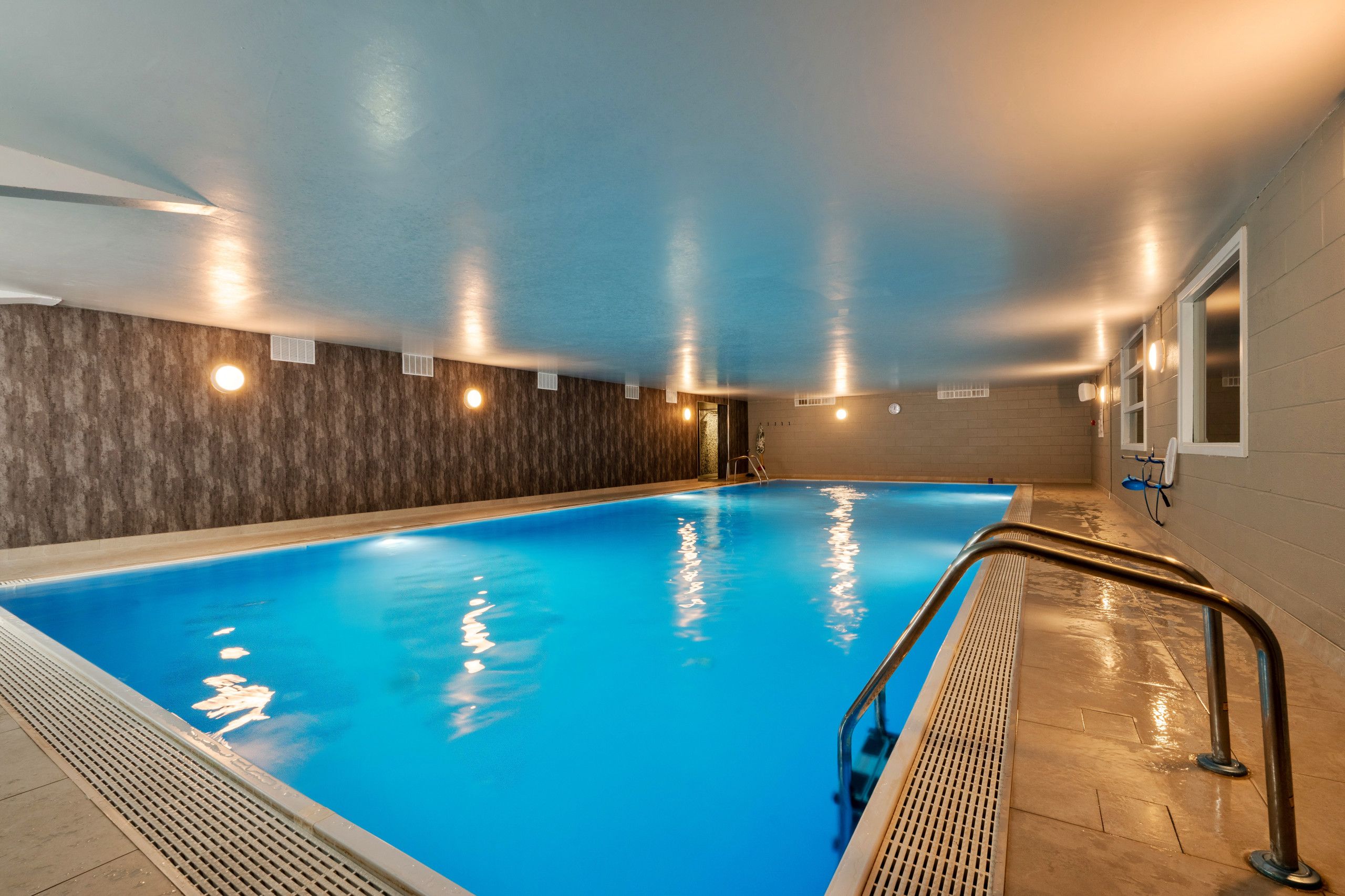 Una piscina interior con superficie de agua azul cristalina, rodeada de paredes con textura y luces empotradas.