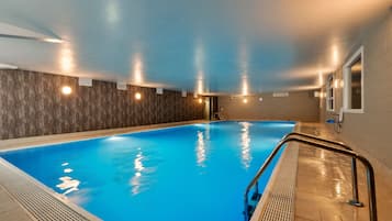 Una piscina interior con superficie de agua azul cristalina, rodeada de paredes con textura y luces empotradas.