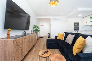 A modern living room with a black sofa, wooden sideboard, and a flat-screen TV. - Deluxe 1-Bedroom Apartment with Panoramic Pool - Happy Place in Faro (Faro)