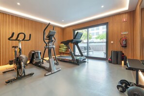 A gym with cardio machines, weightlifting equipment, and a large window providing natural light. - Deluxe 1-Bedroom Apartment with Panoramic Pool - Happy Place in Faro (Faro)