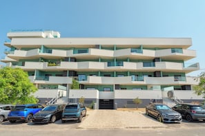 A multi-story building with a modern design, featuring balconies and a parking area with several cars. - Deluxe 1-Bedroom Apartment with Panoramic Pool - Happy Place in Faro (Faro)